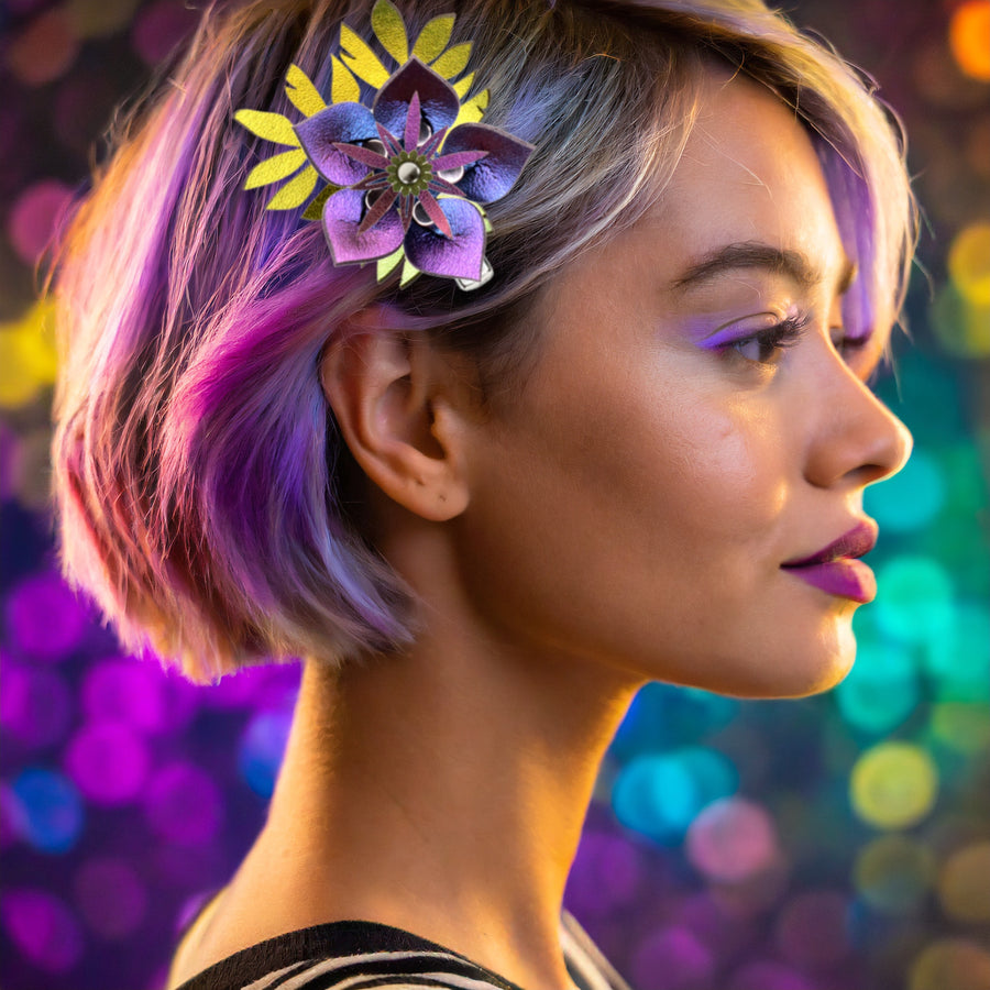 An iridescent blue and purple flower barrette with green-gold iridescent leaves, shown on a woman with violet hair
