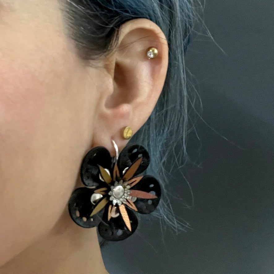 Large earrings with a black flower and red iridescent stamen, shown on a model