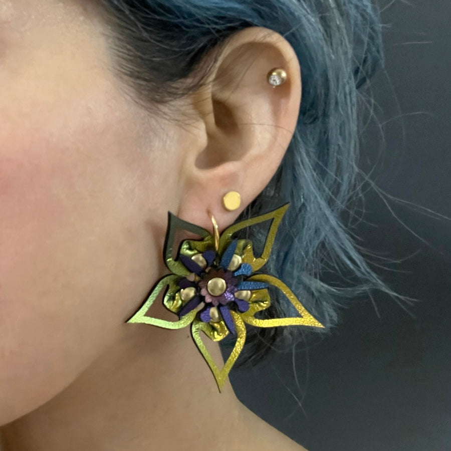 Large earrings with a gold iridescent flower and blue iridescent stamen, shown on a model
