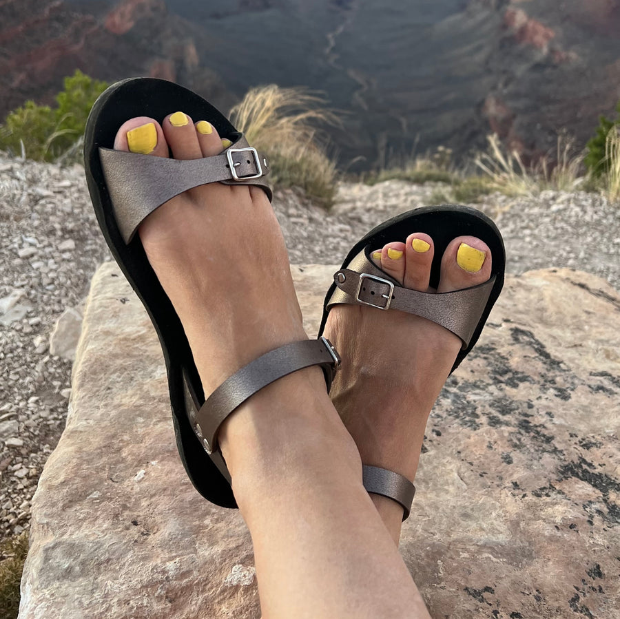 Sandals in rose gold with an ankle strap, shown on a model at the Grand Canyon