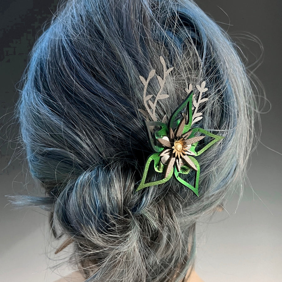 A wood hair stick featuring a large green faux leather flower accented by silver leaves shown on a model