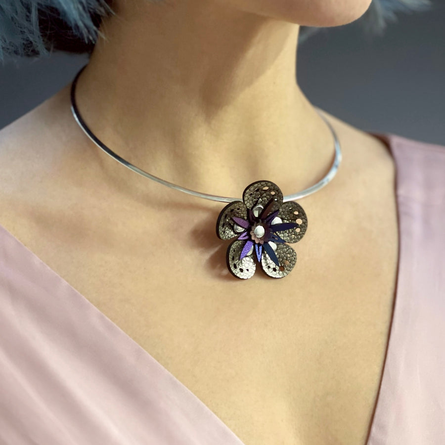 A gold faux leather flower necklace shown on a silver neck wire , worn on a model
