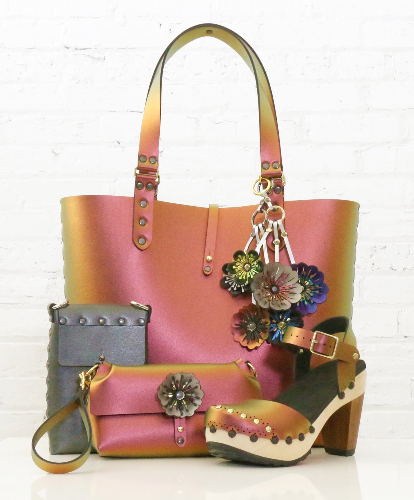 A product image featuring a tote with flower charms, wristlet, and heeled clogs, all in iridescent red, as well as a small bag in dark silver.