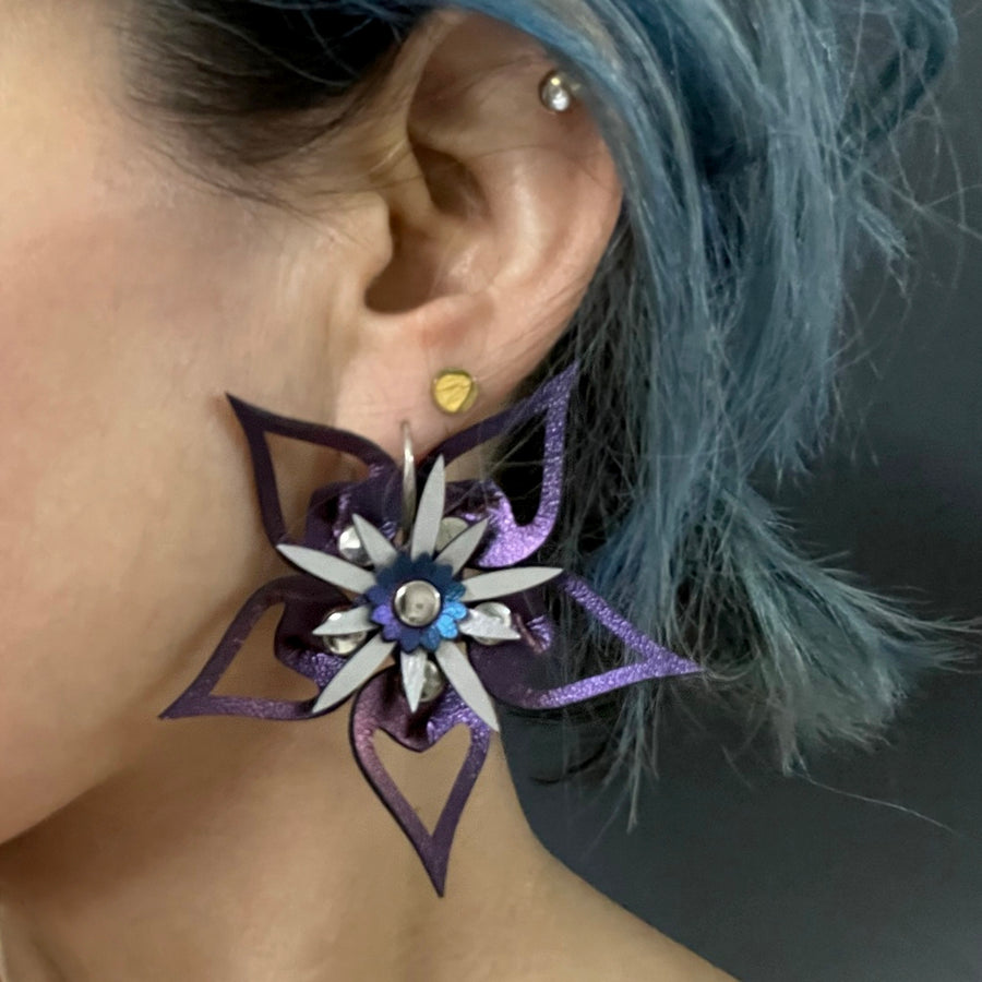 Large earrings with a purple iridescent flower and silver stamen, shown on a model