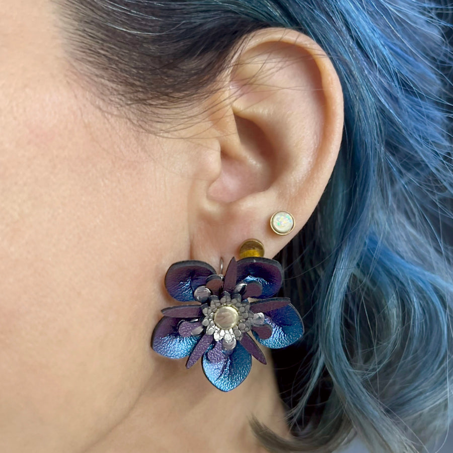 Small iridescent blue faux leather flower earrings shown on a model