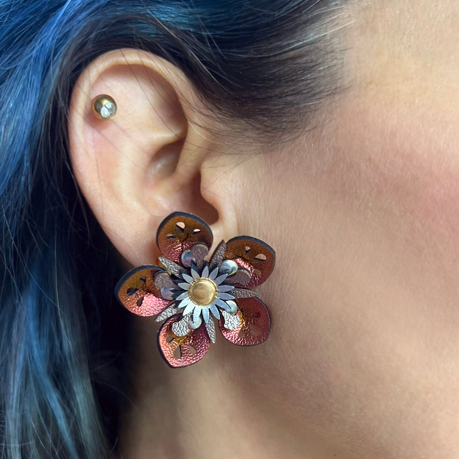 Small iridescent red faux leather flower earrings shown on a model
