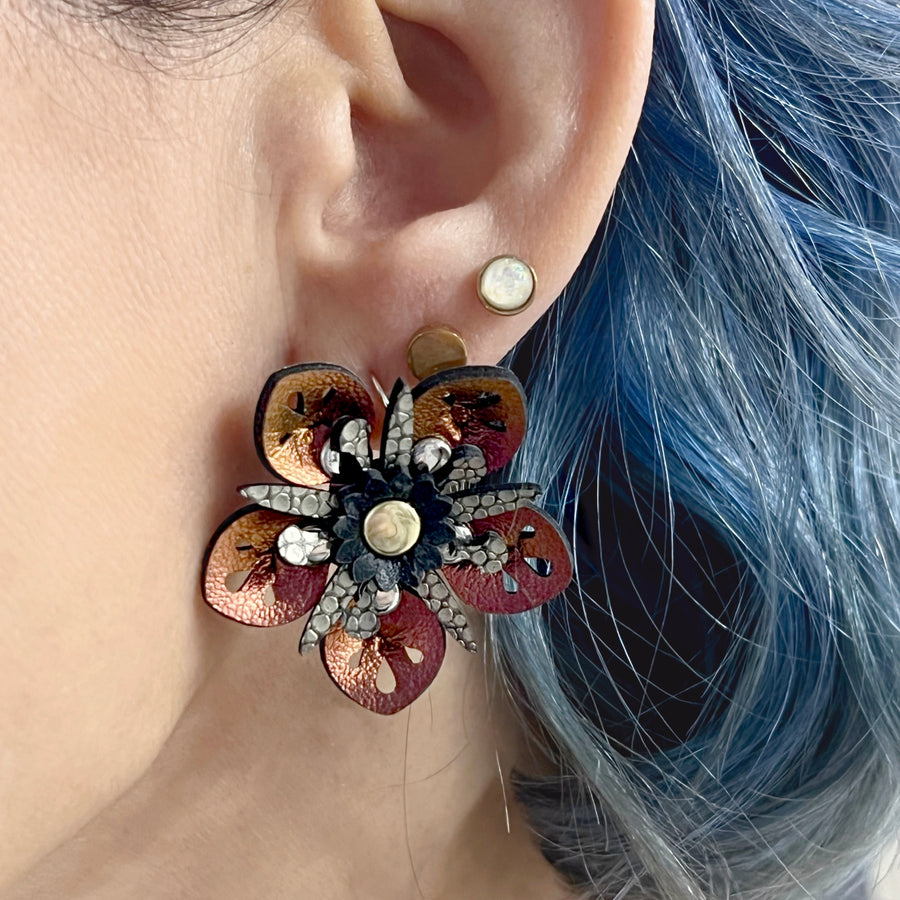 Small iridescent red faux leather flower earrings shown on a model