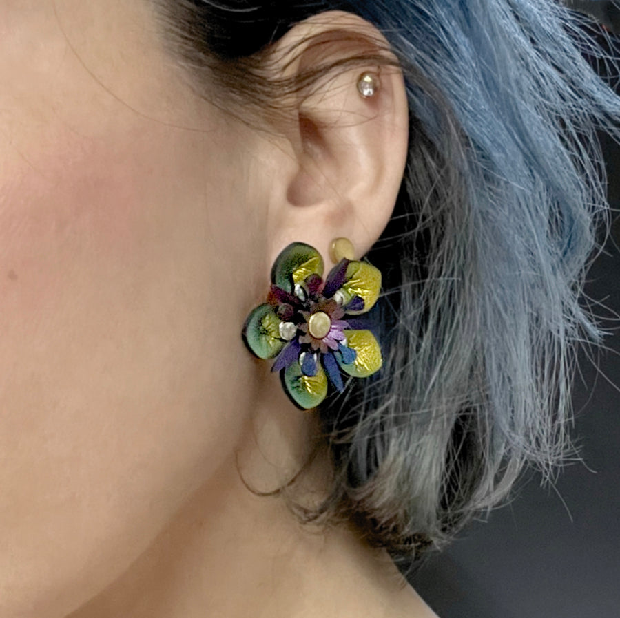 Small iridescent gold faux leather flower earrings shown on a model