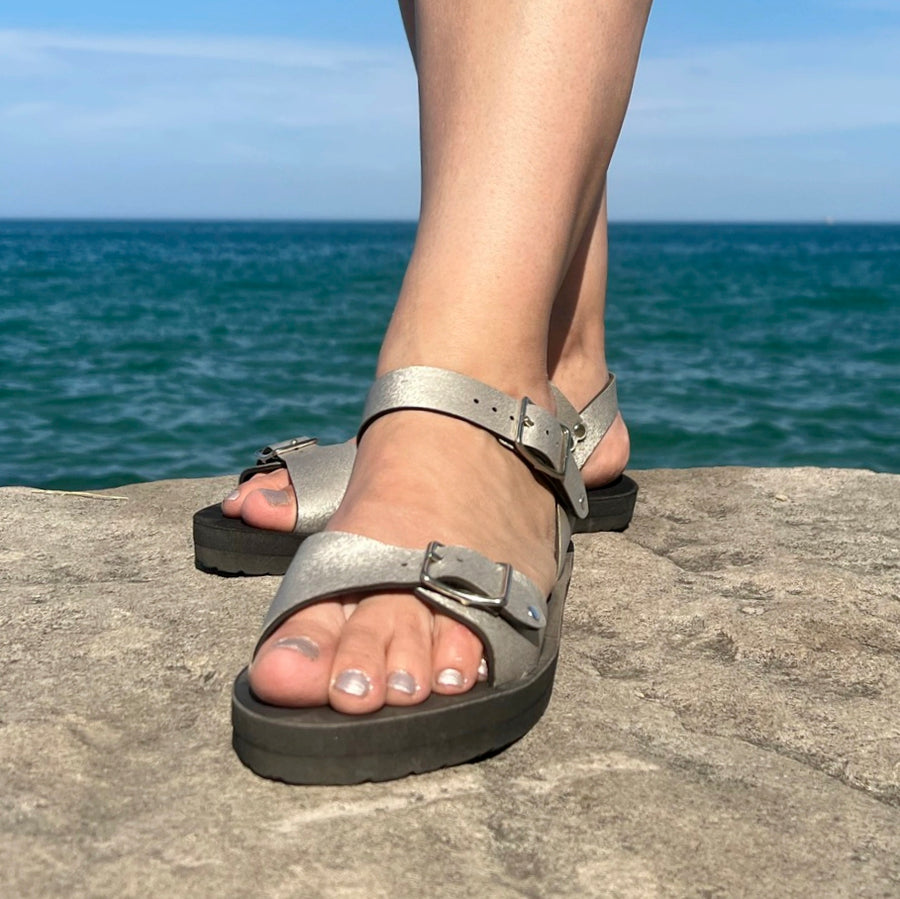 Ankle strap sandals in champagne color, shown on a model standing on a rock on the shore of Lake Michigan