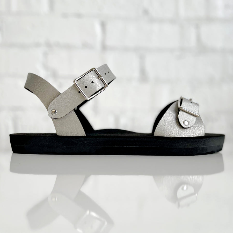 Side view of a flat, padded vegan sandal in champagne color with an ankle strap