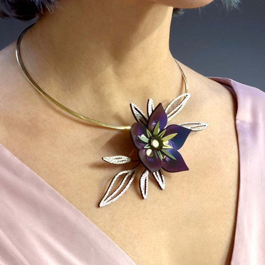 A blue iridescent faux leather flower necklace with gold leaves shown on a silver neck wire, worn on a model