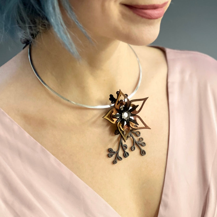 A red iridescent faux leather flower necklace with black leaves shown on a silver neck wire , worn on a model