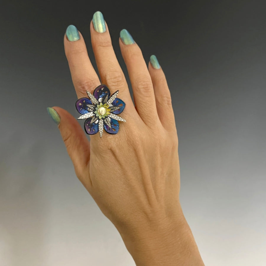 A faux leather ring with a blue iridescent flower and gold stamen on a model's hand
