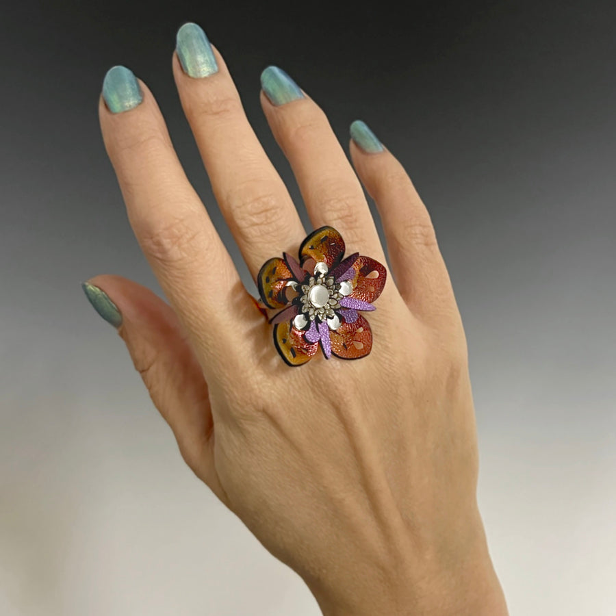 A faux leather ring with a red iridescent flower and purple iridescent stamen on a model's hand