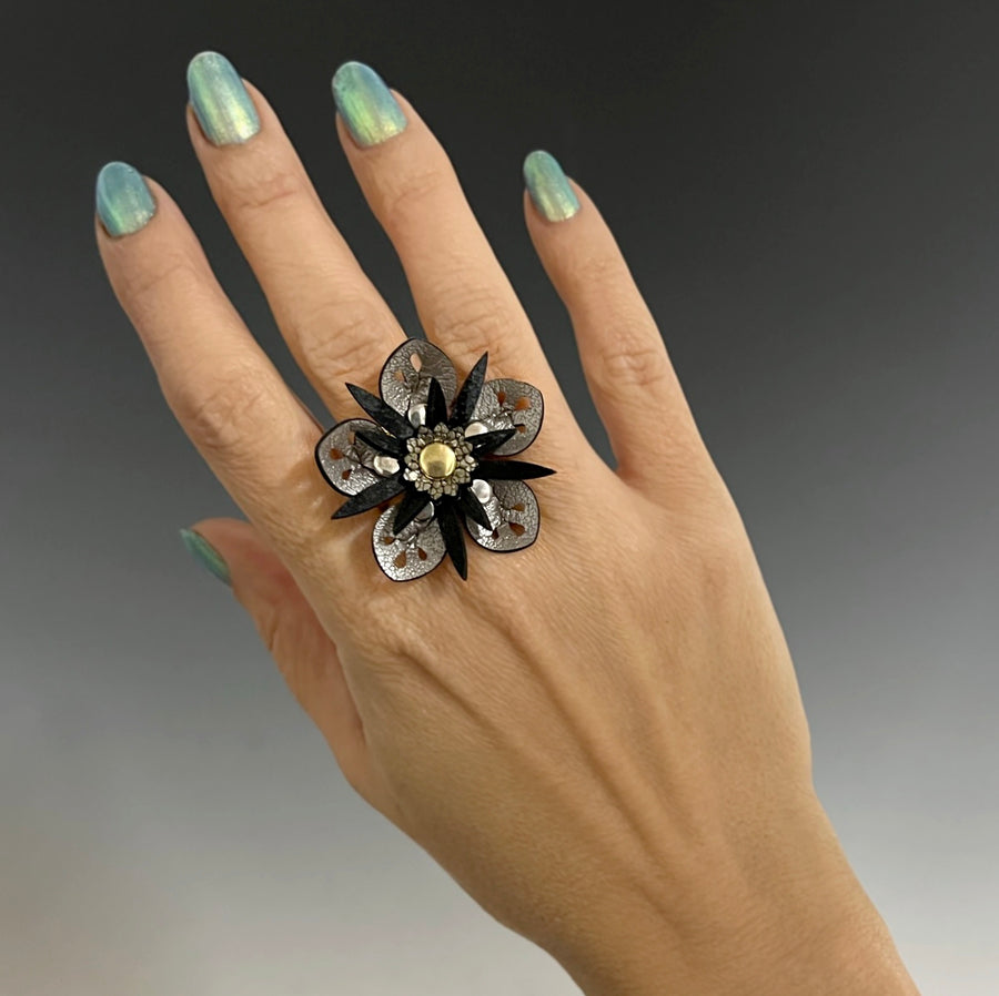 A faux leather ring with a silver flower and black stamen on a model's hand