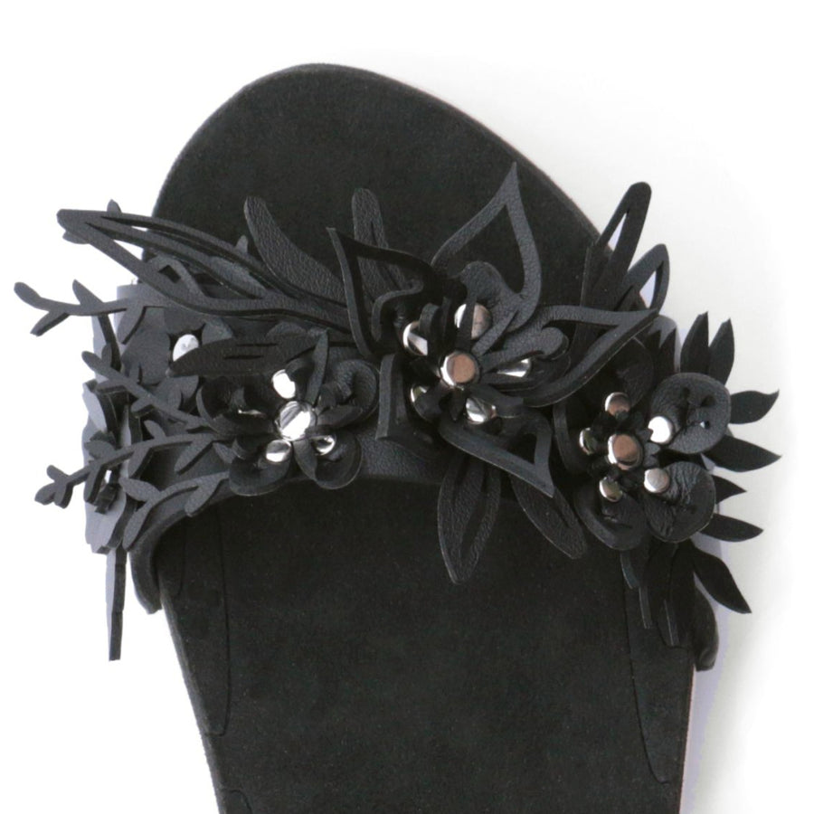 Close up view of a sandal with laser cut flowers in matte black