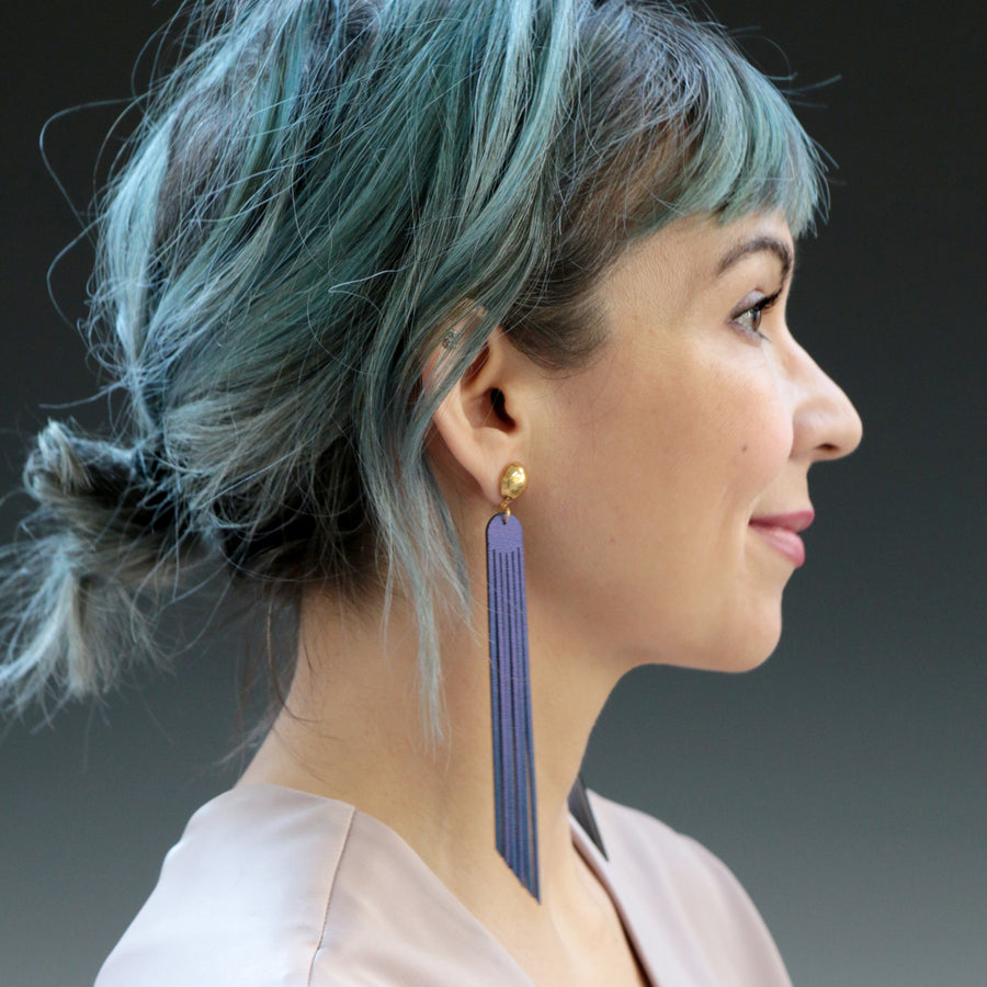 Long iridescent blue fringe earrings with a bright gold post shown on a model