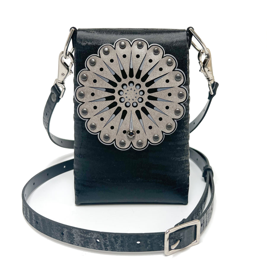 A small bag in black shagreen  vegan leather with a laser cut front flap and adjustable crossbody strap
