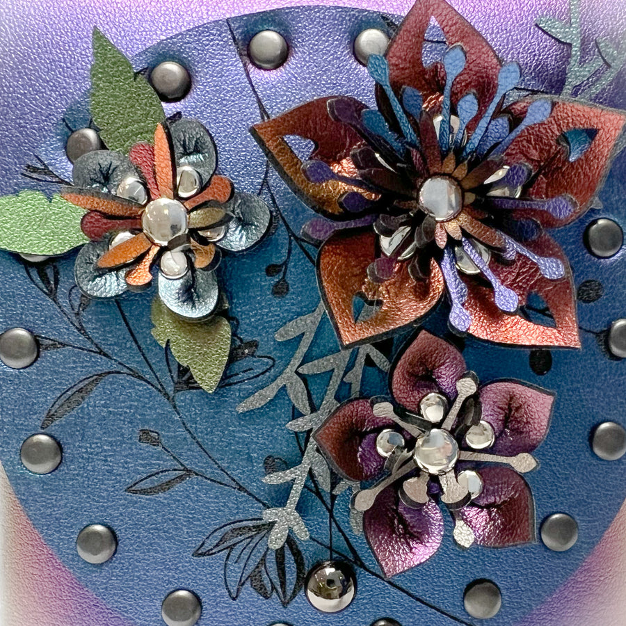 Detail shot of a small bag in blue iridescent vegan leather with a 3D floral laser cut front flap