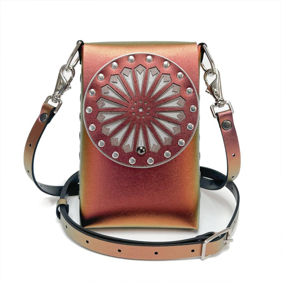 A small bag in red iridescent faux leather with a laser cut front flap and adjustable crossbody strap