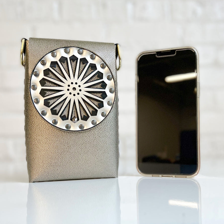 A small bag in gold vegan shagreen with a laser cut front flap and adjustable crossbody strap, shown next to an iphone 13 max for size comparison
