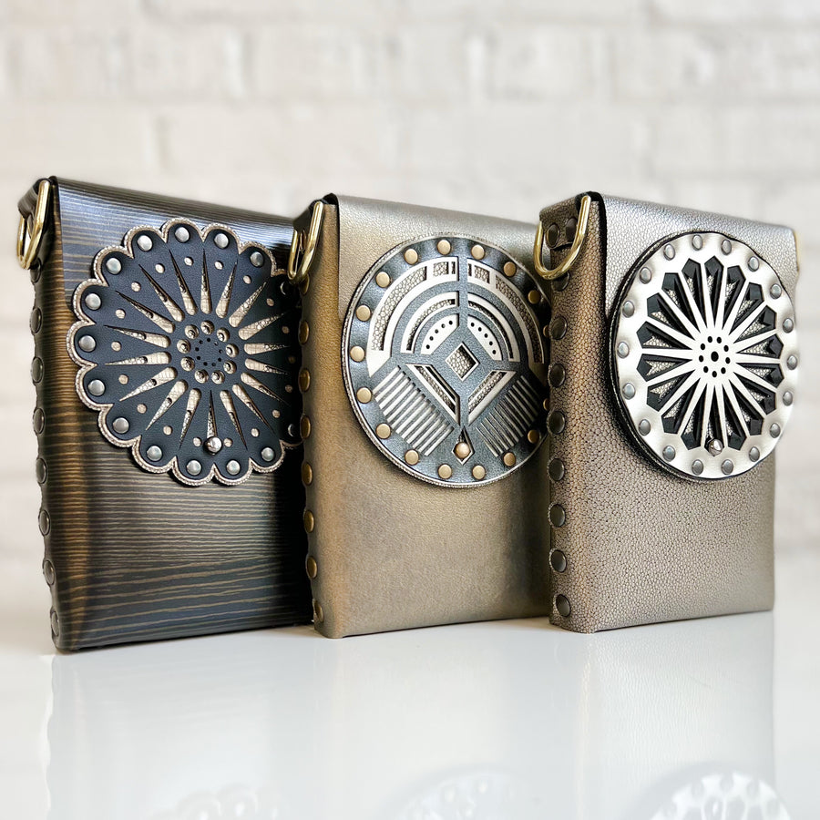 Three small vegan bags in various shades of browns, blacks and golds. Each bag has an intricate laser cut decorative front flap.