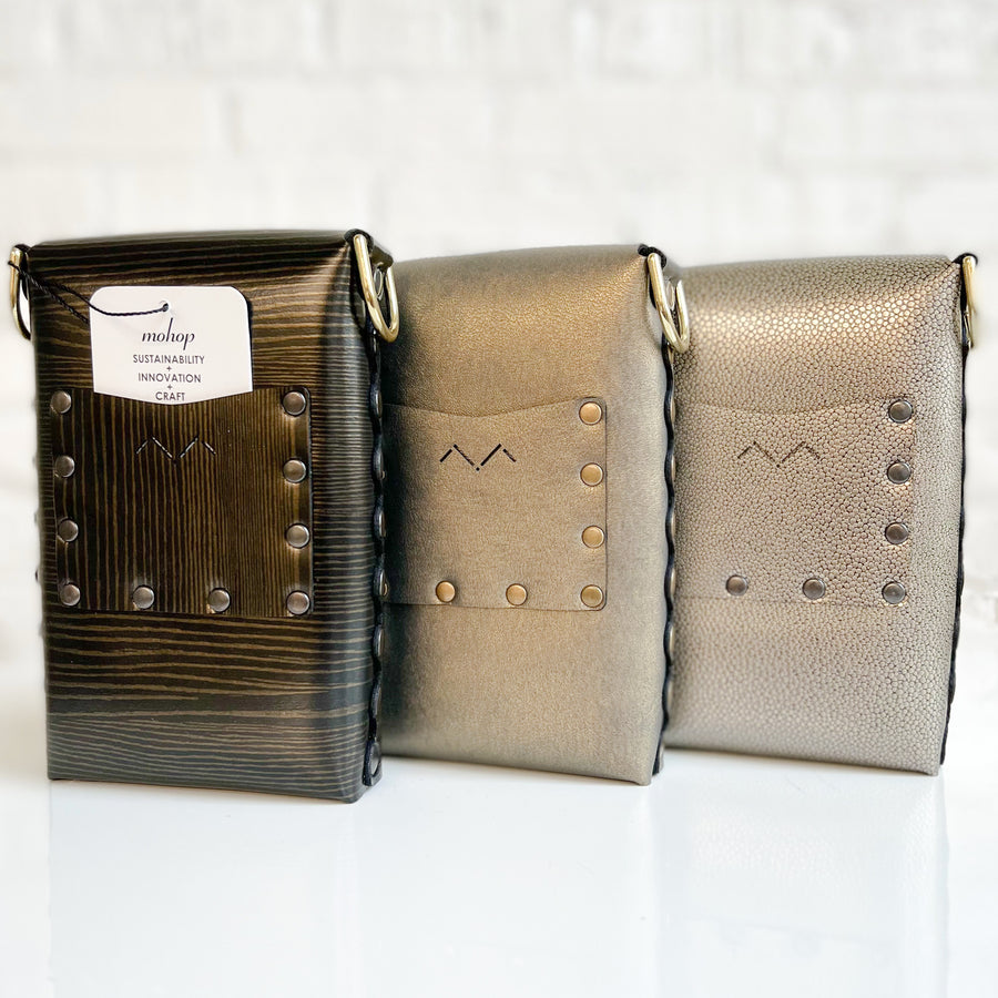 A back view of three small vegan bags in various shades of browns, blacks and golds. Each bag has small card-sized pocket on the back