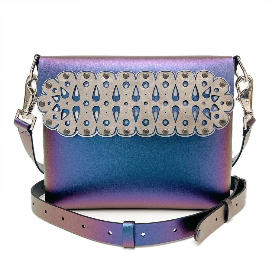 A front shot, including strap, of a square crossbody bag in iridescent blue vegan faux leather with a laser cut front