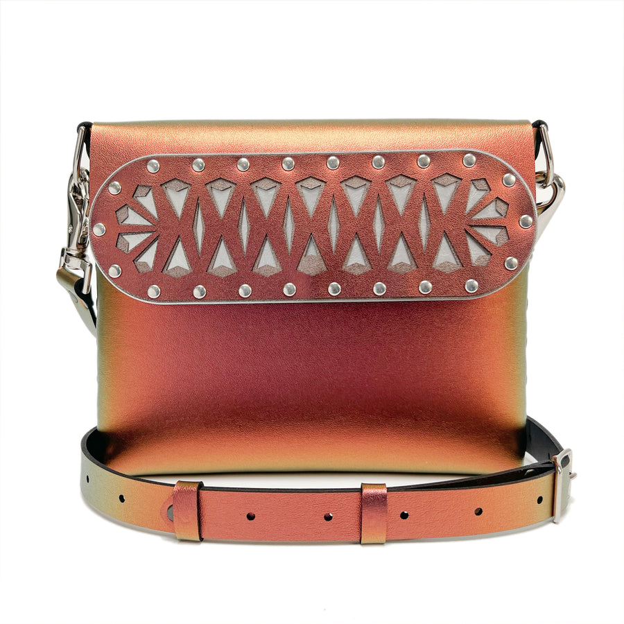 A front shot, including strap, of a square crossbody bag in iridescent red vegan faux leather with a laser cut front